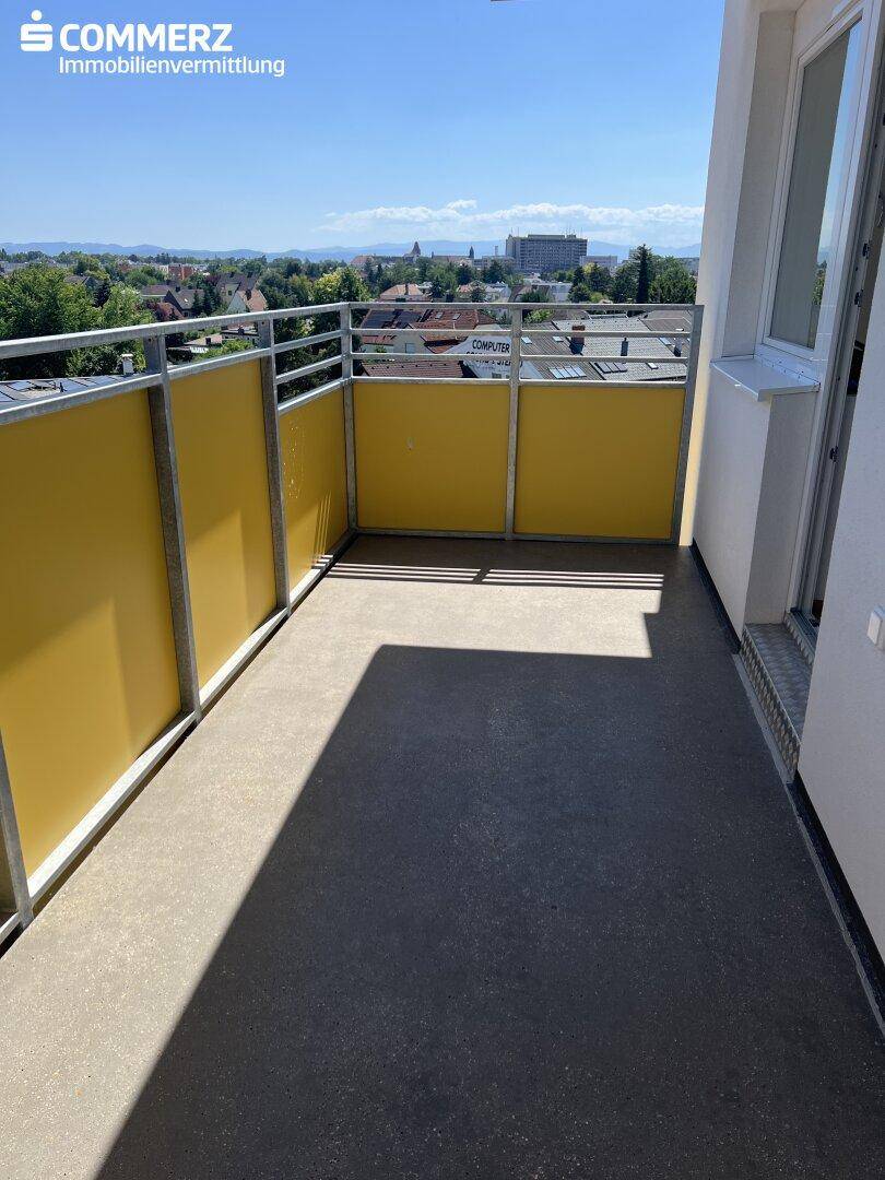 Sonniger Balkon mit gelben Brüstungselementen und weitem Blick über die Stadt.