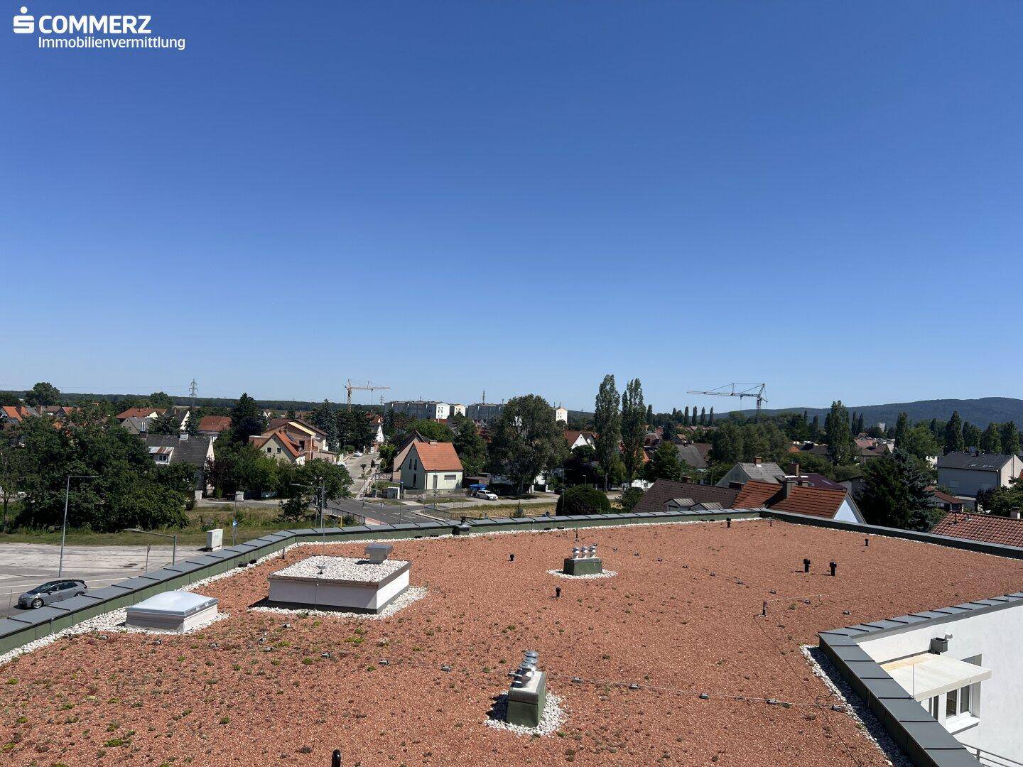 Dachlandschaft eines Gebäudes mit Blick auf die umliegende Wohngegend und Berge.