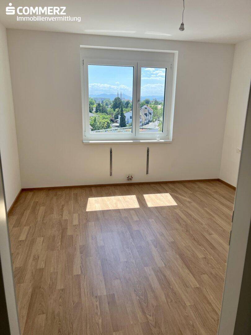 Helles Schlafzimmer mit Laminatboden und großem Fenster mit Blick ins Grüne.