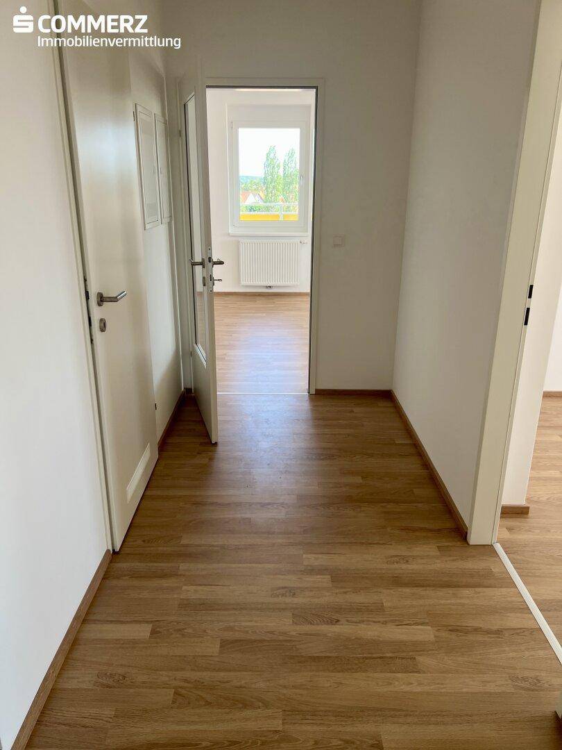 Flur mit Laminatboden, der zu einem weiteren hellen Raum mit Fenster führt.
