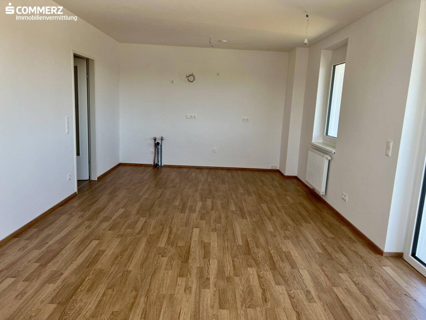 Geräumiges Wohnzimmer mit Laminatboden und Anschlüssen für eine offene Küche.