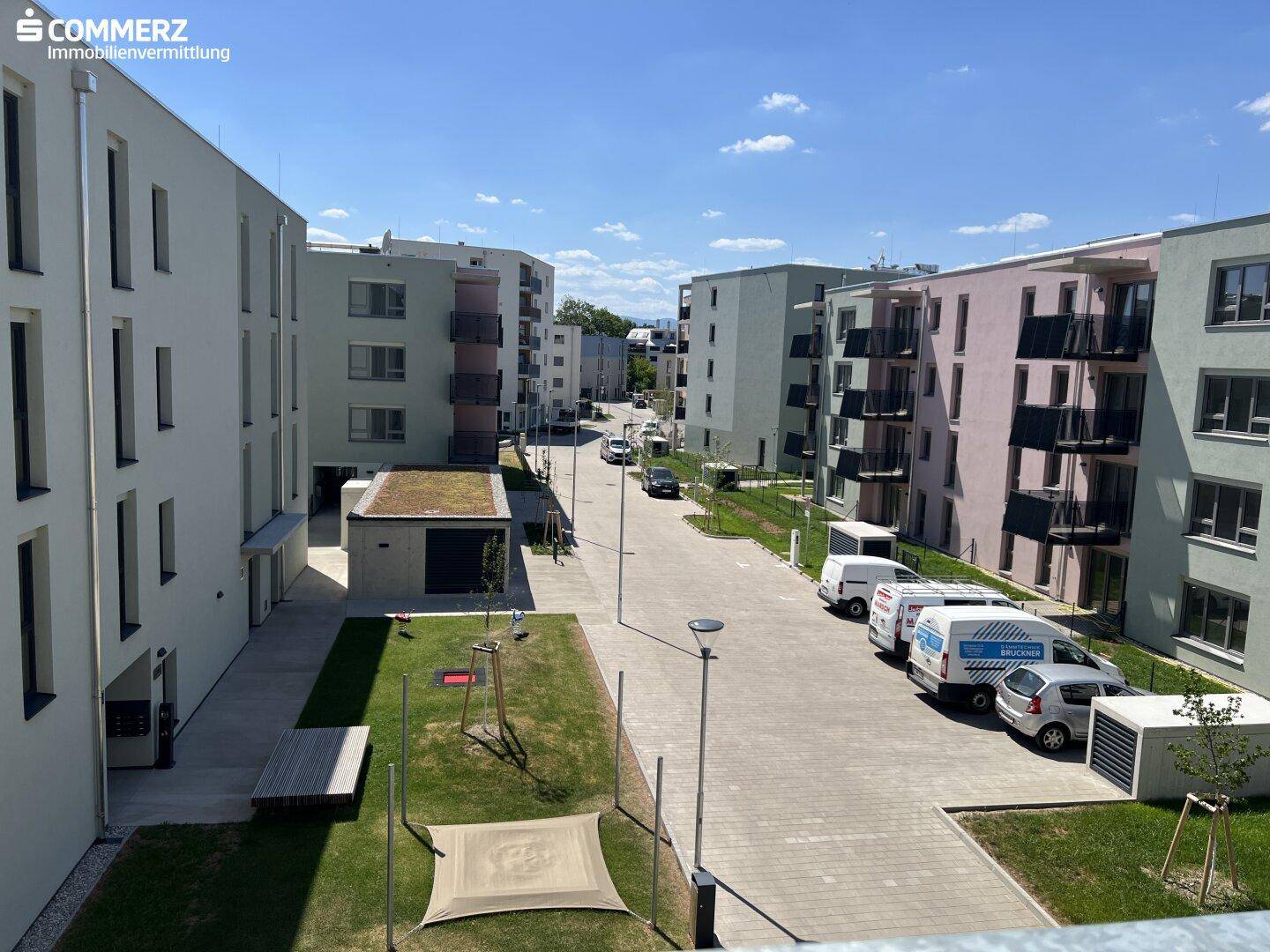 Außenansicht einer modernen Wohnanlage mit mehreren Gebäuden, Grünflächen und einer Straße.