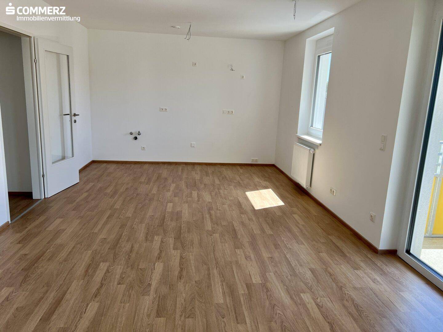 Heller Raum mit Laminatboden und Anschlüssen für eine Küche, bereit für die Installation.
