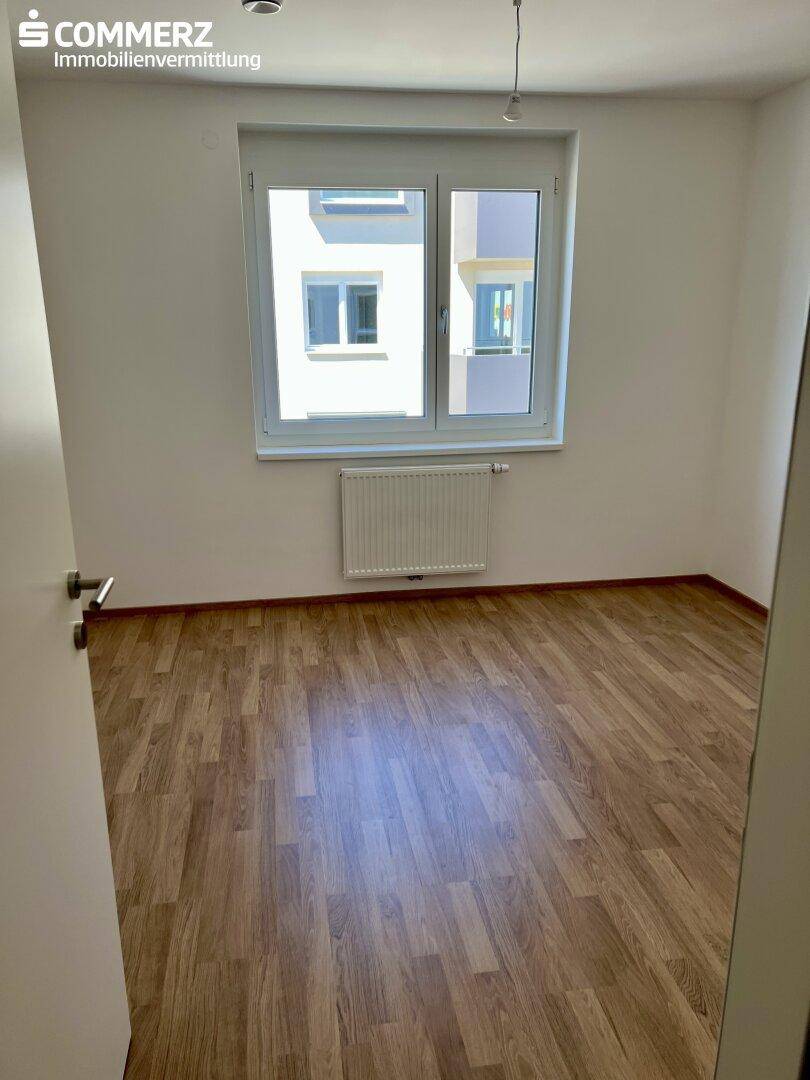 Schlafzimmer mit Laminatboden, weißen Wänden und einem großen Fenster für viel Tageslicht.