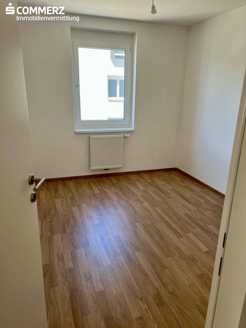 Weiteres Schlafzimmer mit Laminatboden, weißen Wänden und einem Fenster, das Tageslicht hereinlässt.