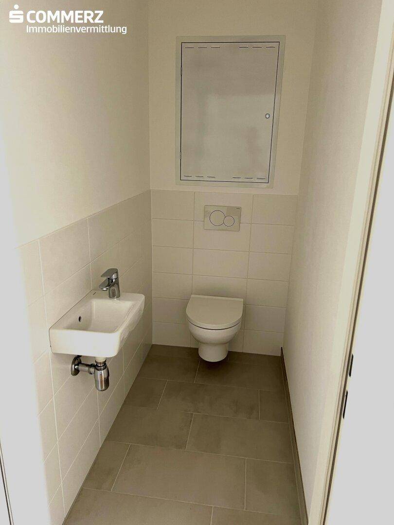 Separates Gäste-WC mit weißen Fliesen, wandhängender Toilette und kleinem Handwaschbecken.