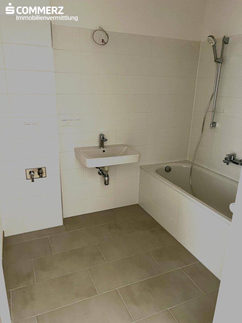 Modernes Badezimmer mit weißen Fliesen, einem Waschbecken und einer Badewanne mit Duschfunktion.