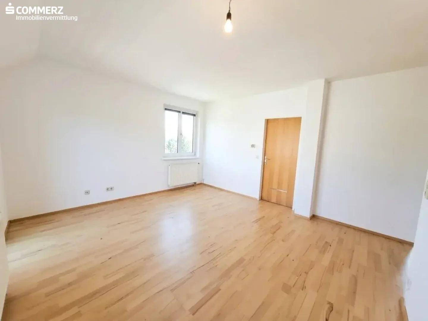 Lichtdurchflutetes Zimmer mit Parkettboden, weiß gestrichenen Wänden und einem Fenster.