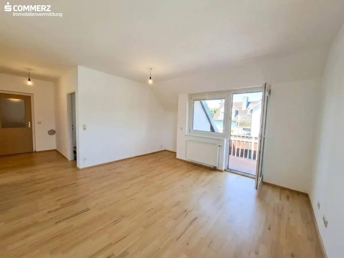 Geräumiges, helles Zimmer mit Parkettboden, weiß gestrichenen Wänden und Balkonzugang.