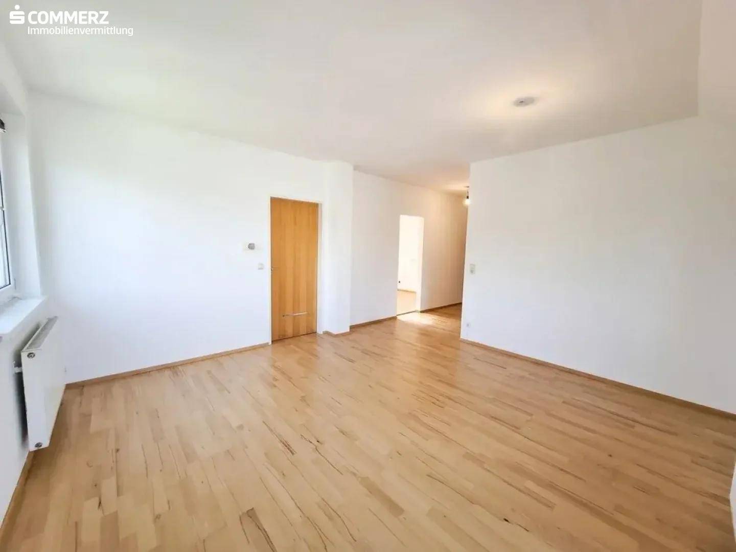 Helles Zimmer mit Parkettboden, weiß gestrichenen Wänden und Blick in den Flur.