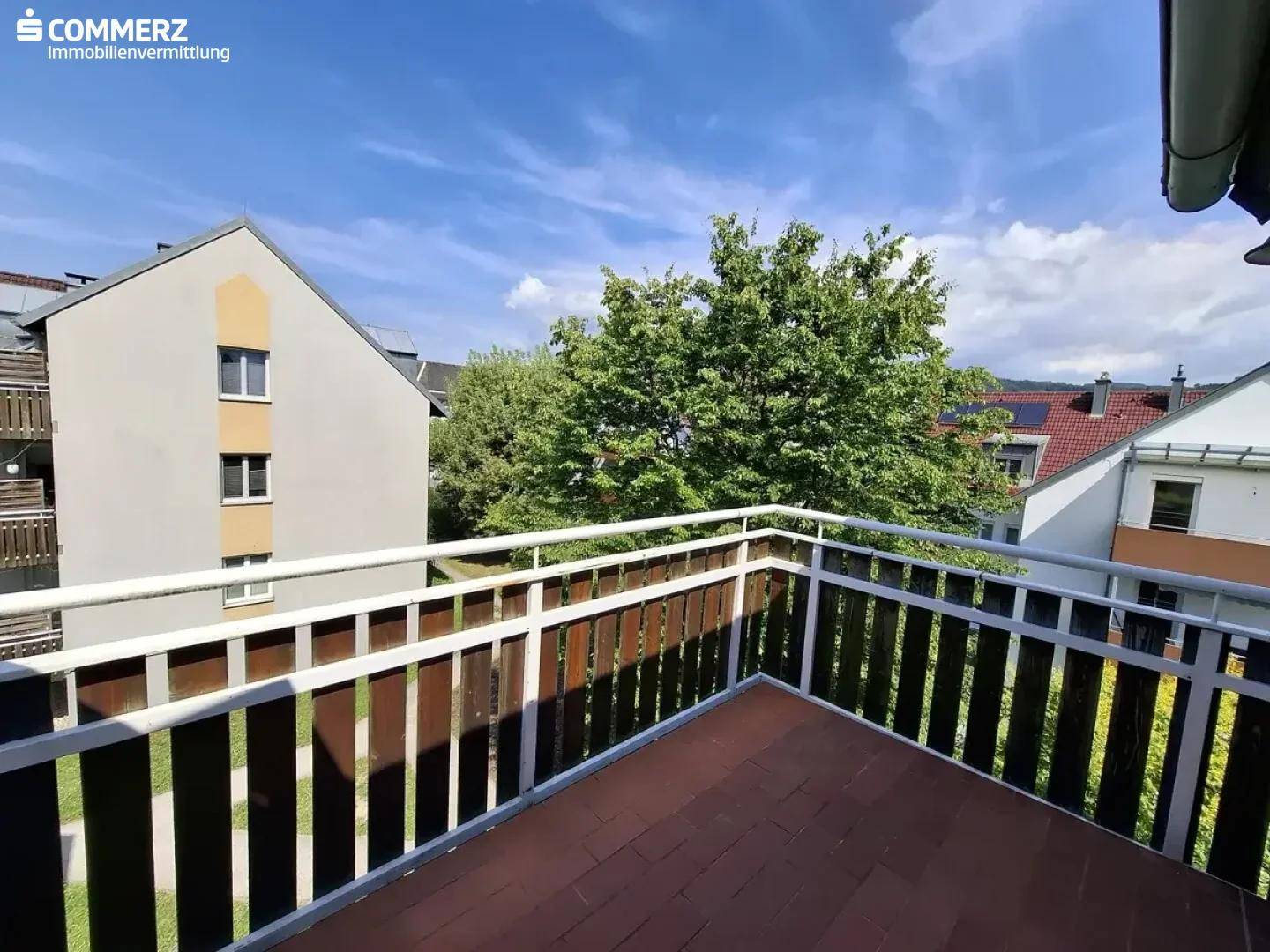 Geräumiger Balkon mit Holzgeländer und Blick auf die umliegenden Gebäude und Bäume.