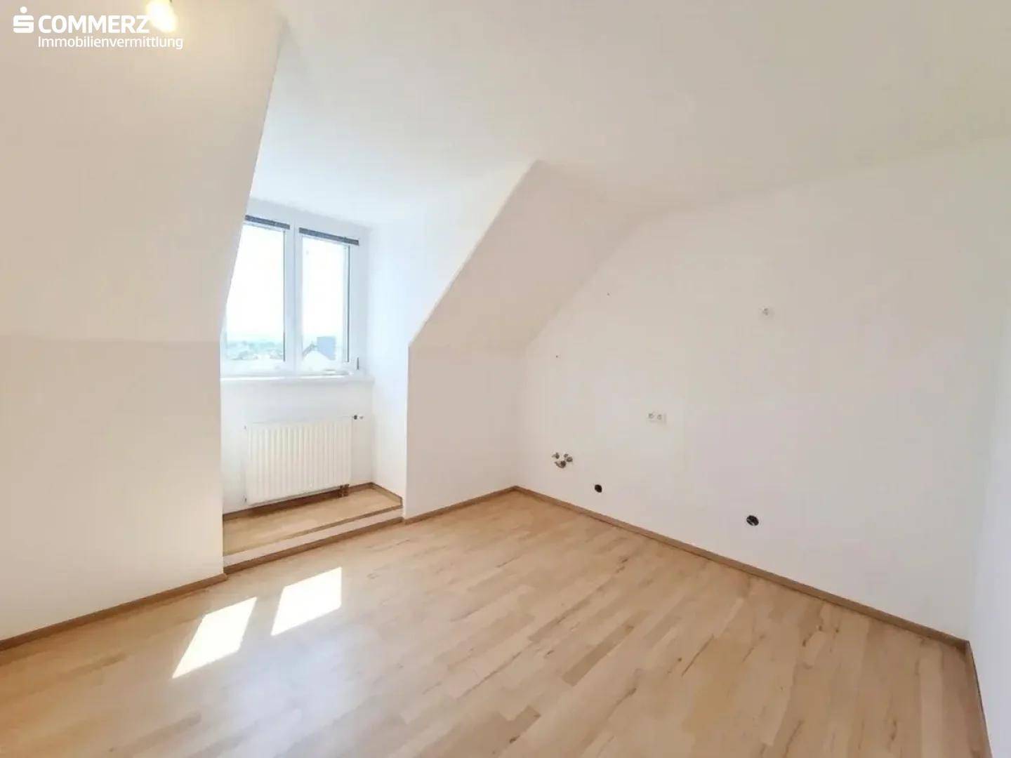 Helles Schlafzimmer im Dachgeschoss mit Parkettboden, Dachschräge und Fenster.