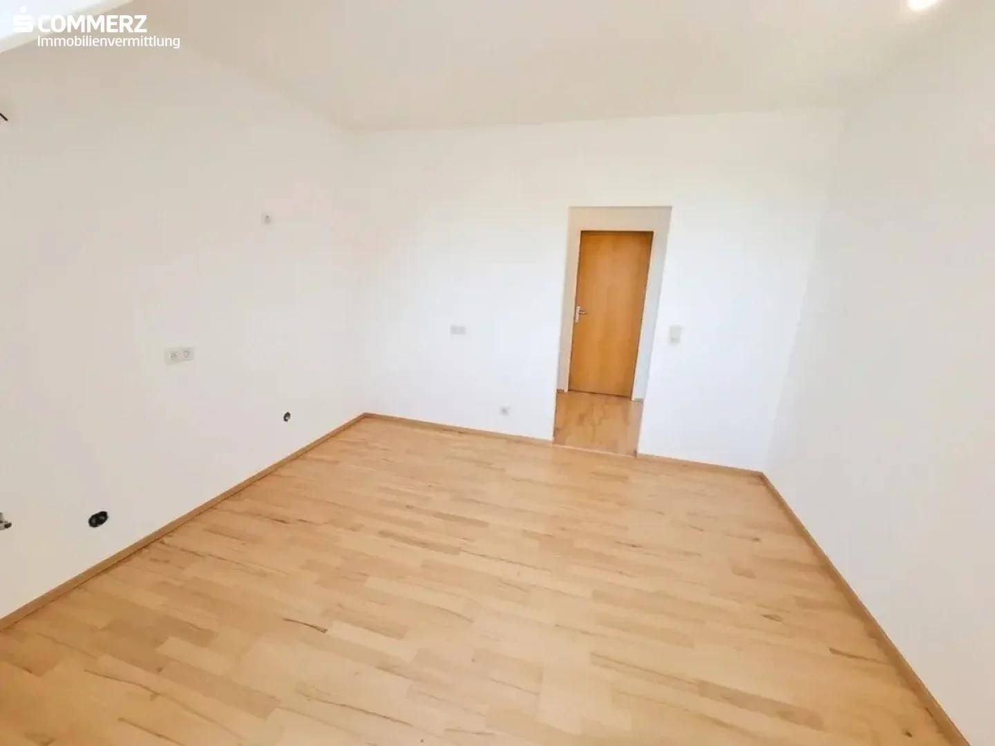 Leeres Zimmer im Dachgeschoss mit Parkettboden, weiß gestrichenen Wänden und Holztür.