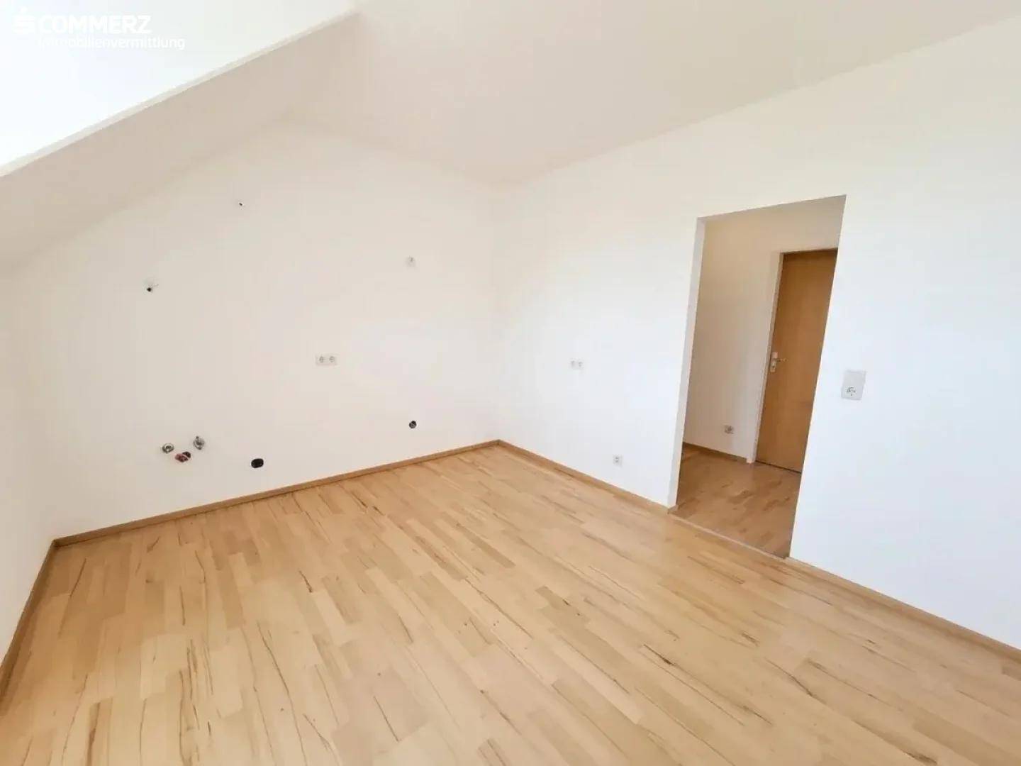 Geräumiges Zimmer im Dachgeschoss mit Parkettboden, Dachschräge und Holztür.