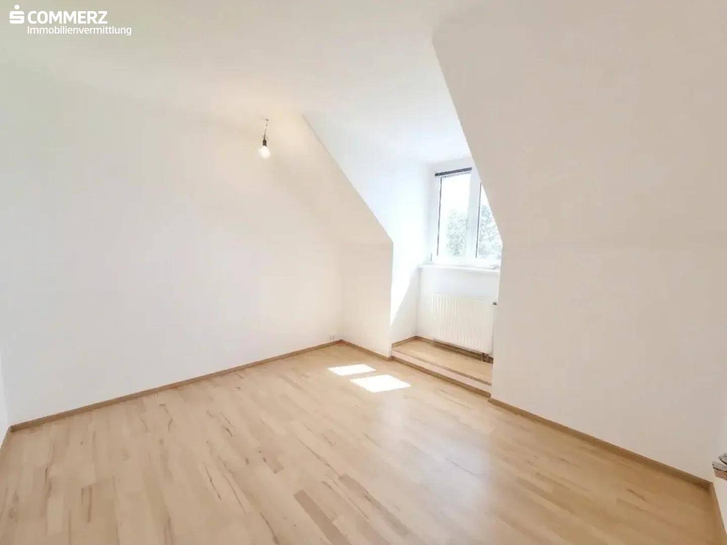 Lichtdurchflutetes Zimmer im Dachgeschoss mit Parkettboden, Dachschräge und Fenster.