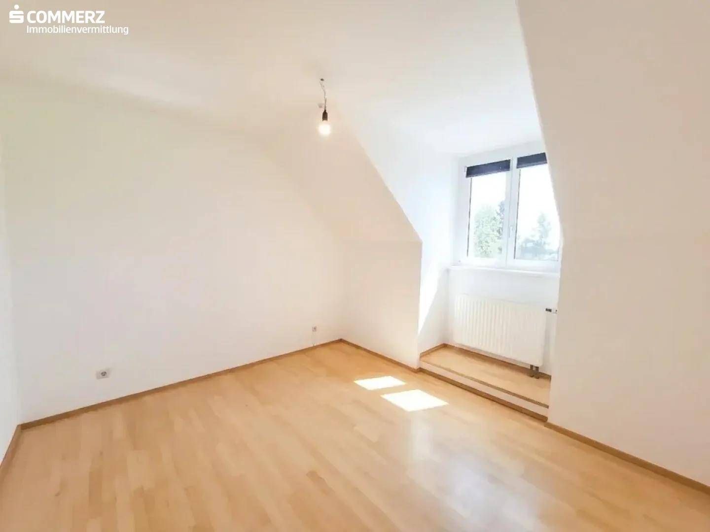 Lichtdurchflutetes Zimmer im Dachgeschoss mit Parkettboden, Dachschräge und Fenster.