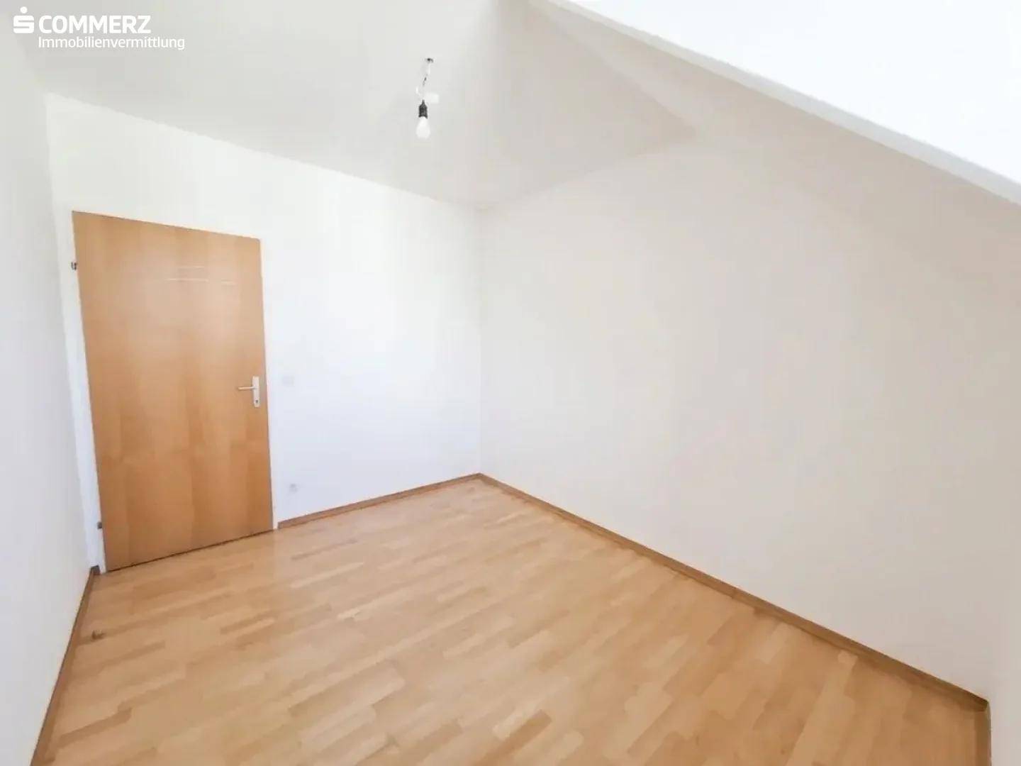Geräumiges Zimmer im Dachgeschoss mit Parkettboden, Dachschräge und Holztür.