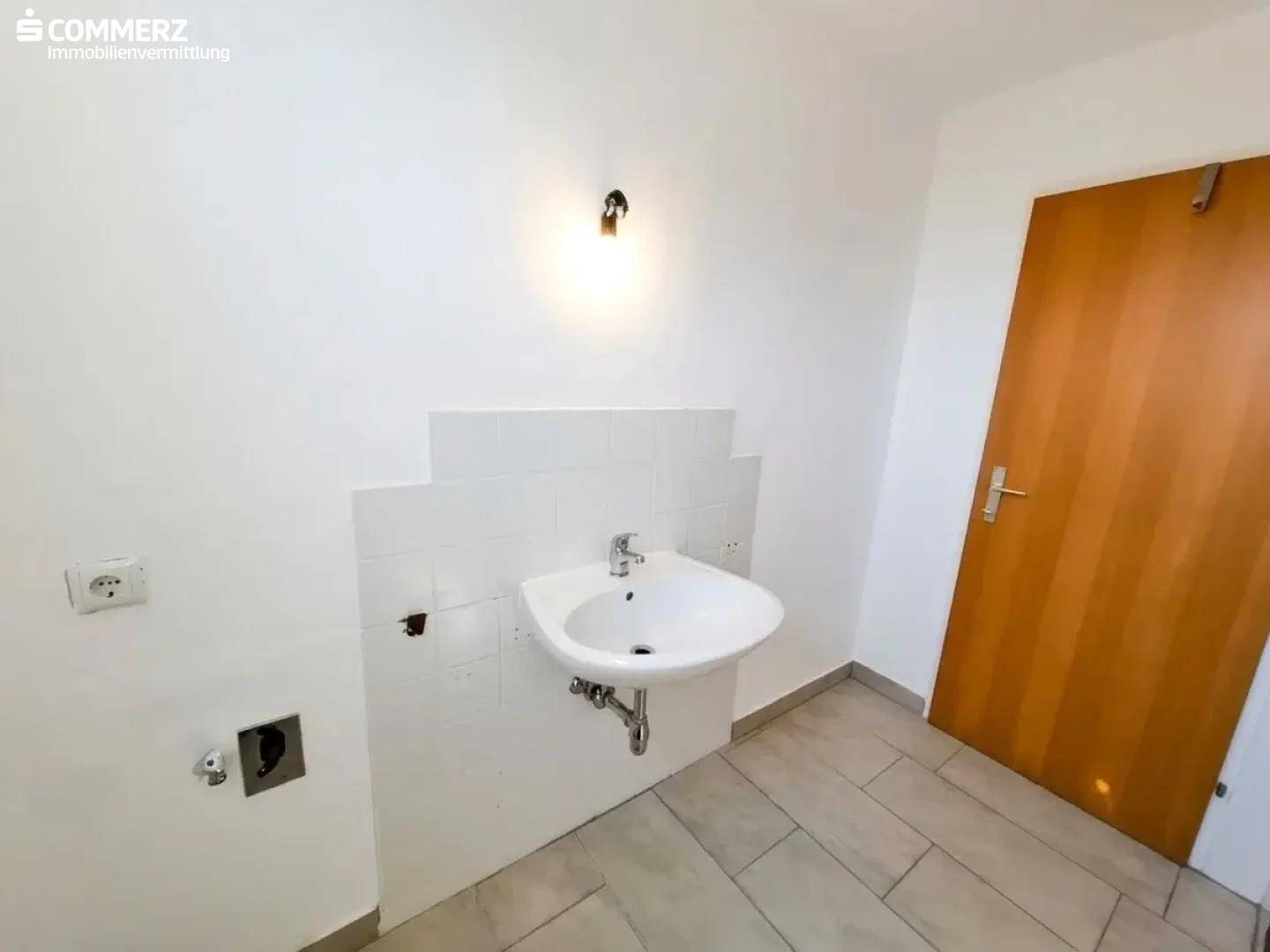 Praktischer Raum mit Waschbecken, Fliesenboden und Anschlüssen für Waschmaschine.