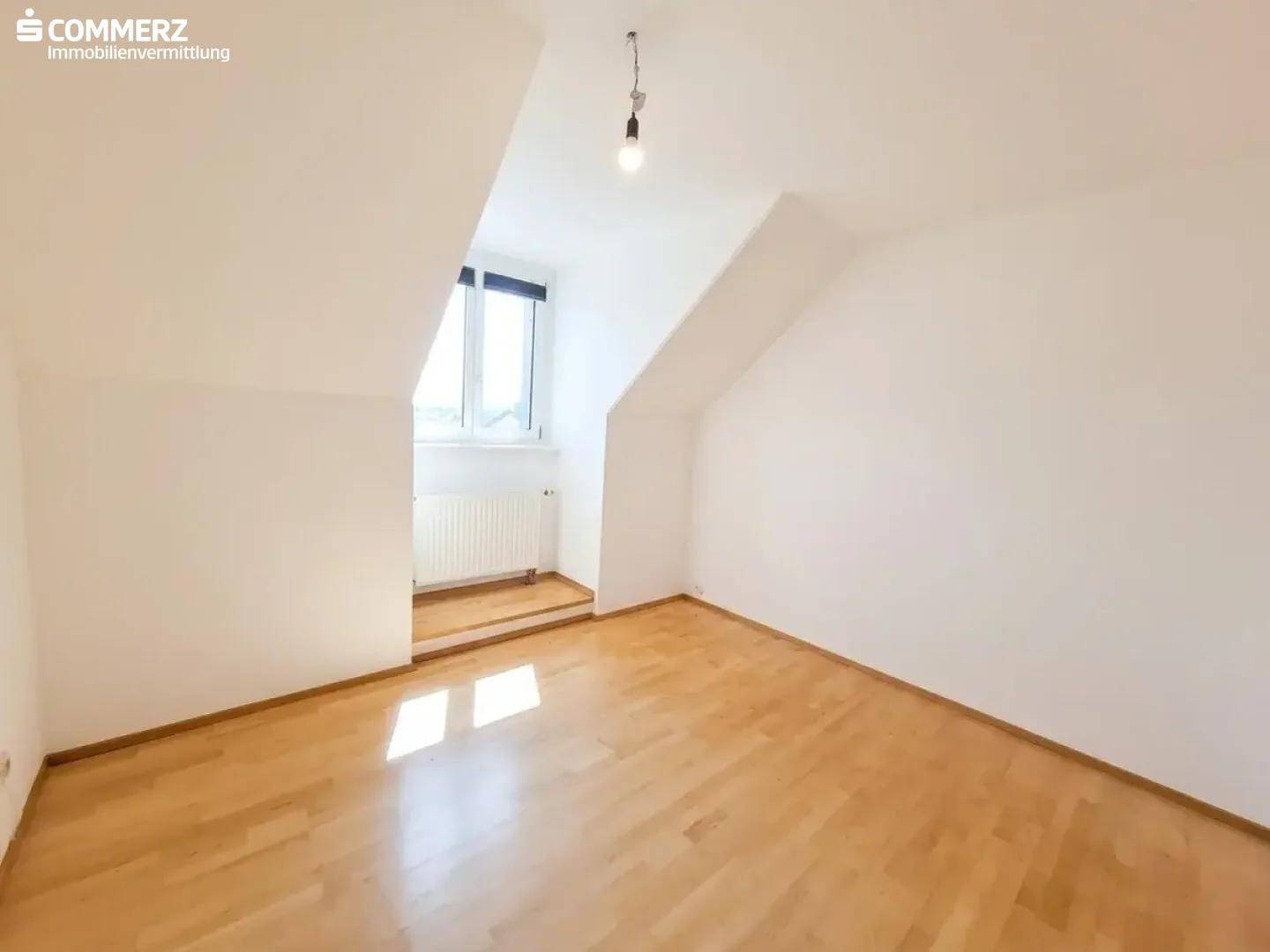 Helles Zimmer im Dachgeschoss mit Parkettboden, Dachschräge und Fenster.