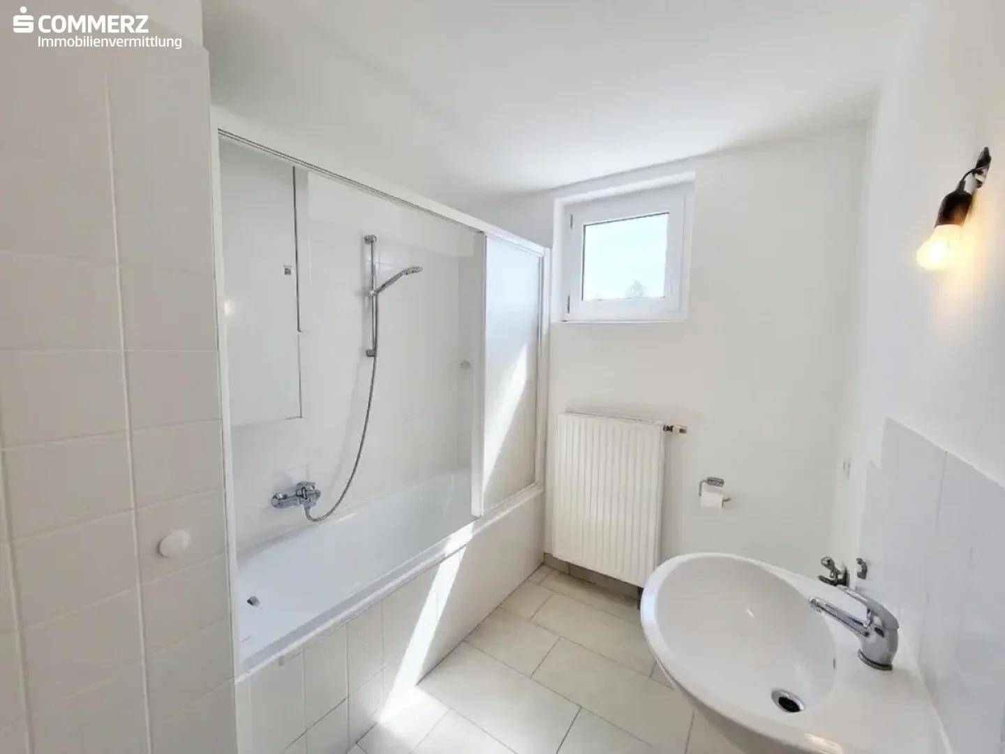 Modernes Badezimmer mit Badewanne, Duschabtrennung, Waschbecken und Fenster.