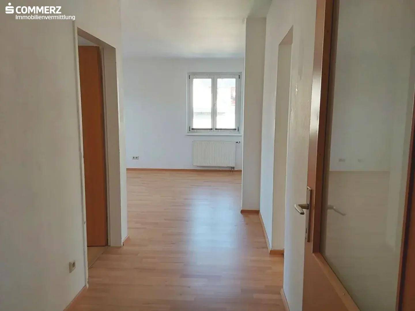 Heller Flur mit Parkettboden, weiß gestrichenen Wänden und Blick in ein Zimmer.