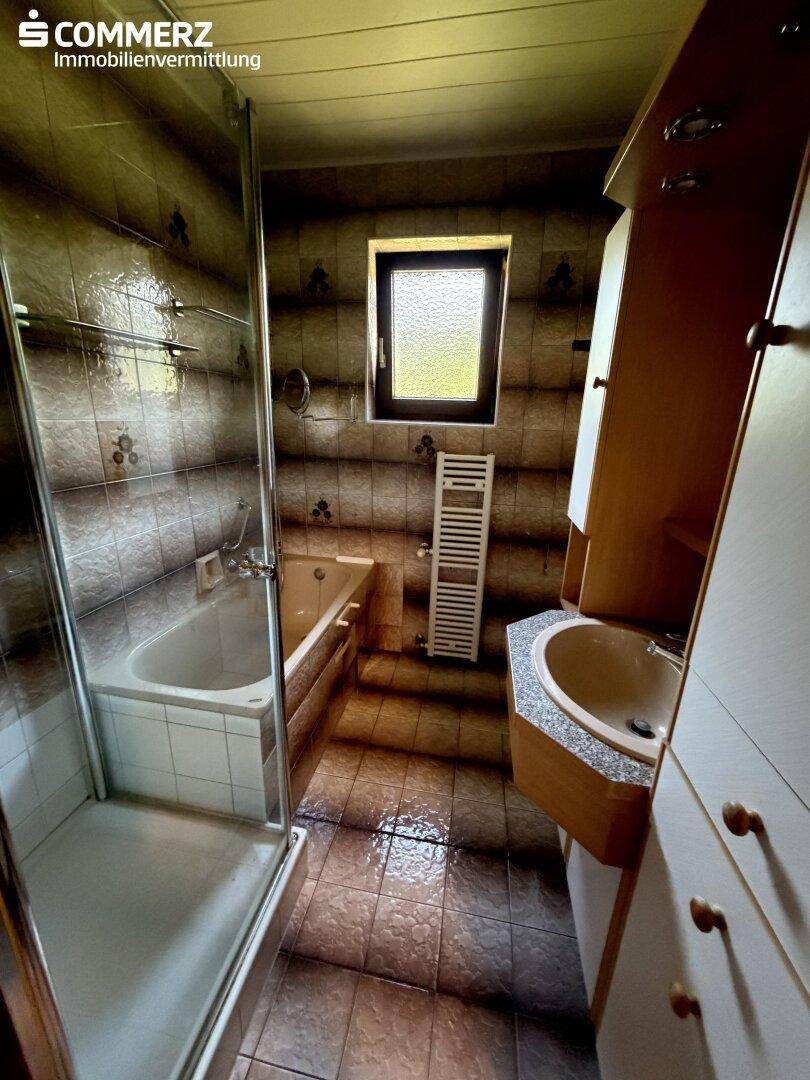 Badezimmer mit Badewanne, Dusche, Waschbecken und Fenster.