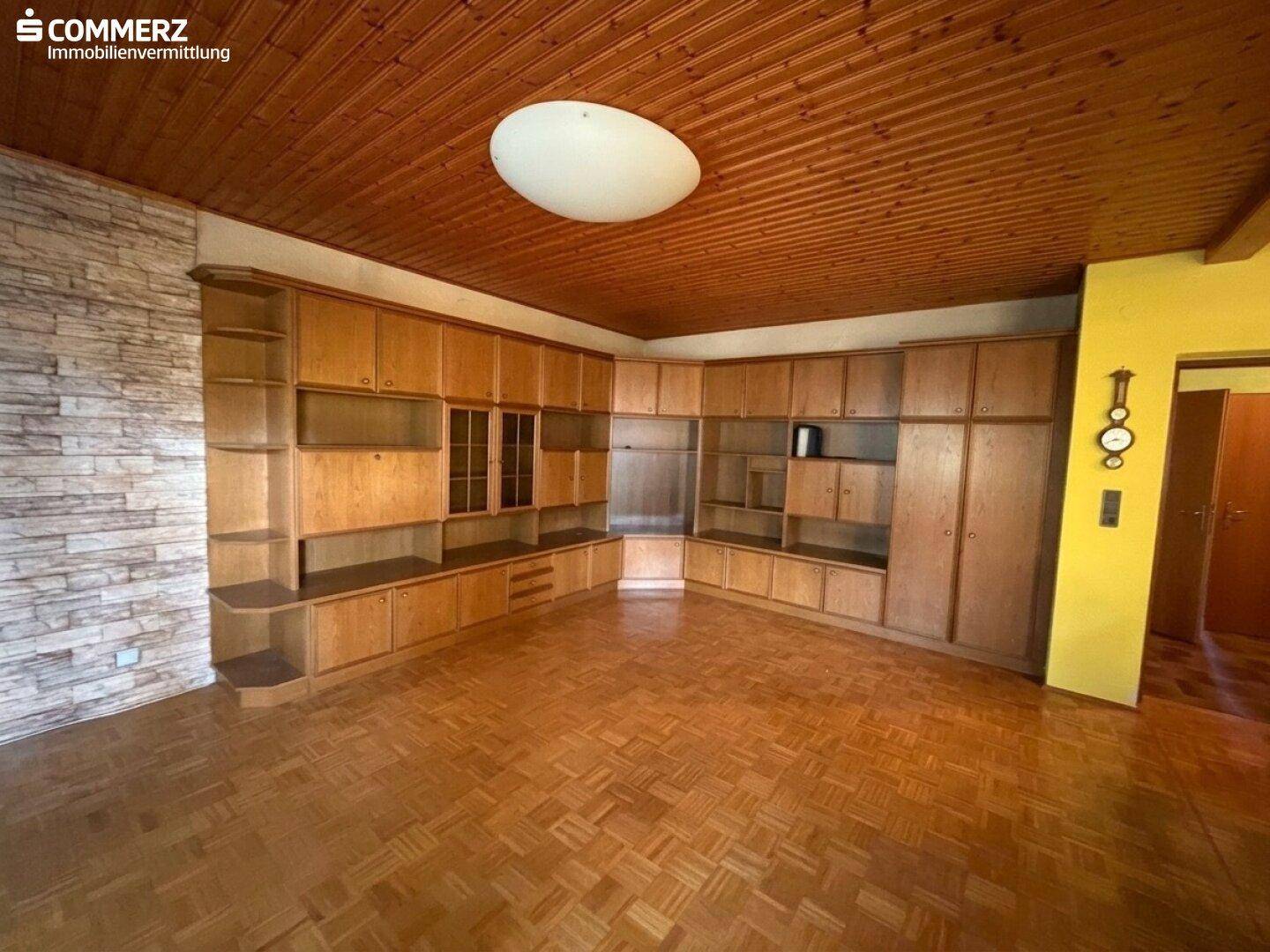 Geräumiges Wohnzimmer mit Holzdecke, Parkettboden und großer Einbauschrankwand.