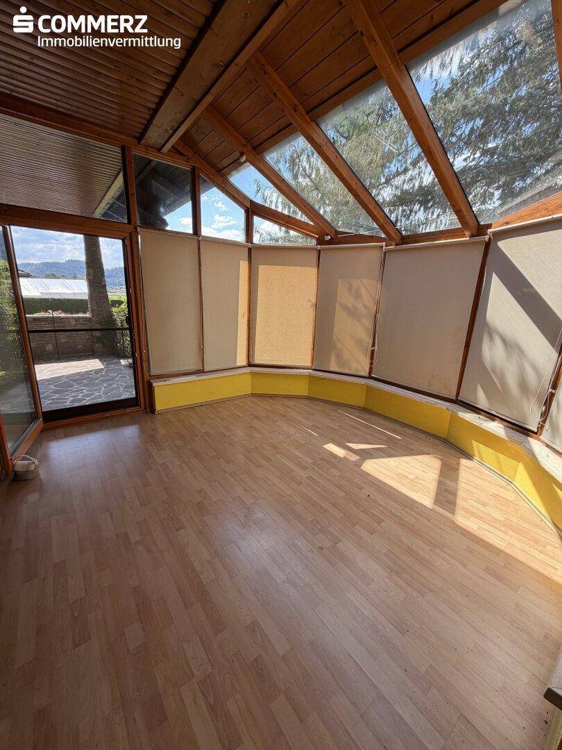 Heller Wintergarten mit Holzdecke, großen Glasflächen und Blick in die Natur.