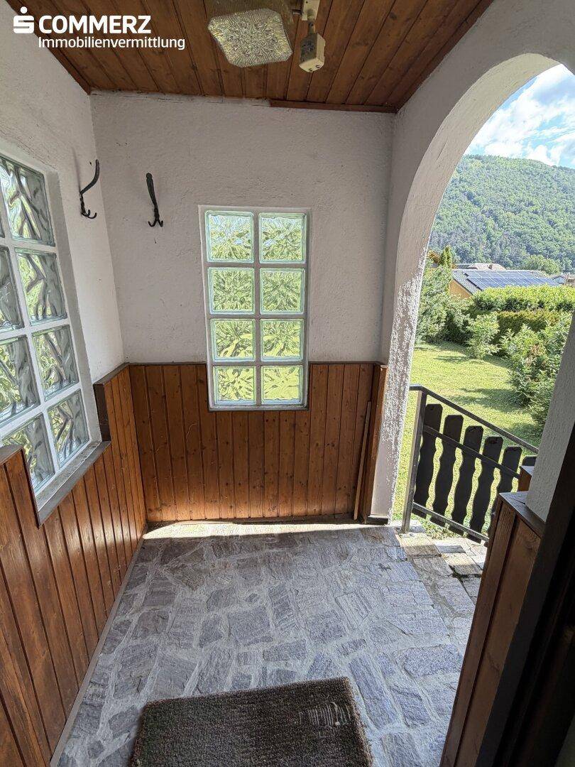 Überdachter Eingangsbereich mit Steinboden, Holzvertäfelung und Blick ins Grüne.