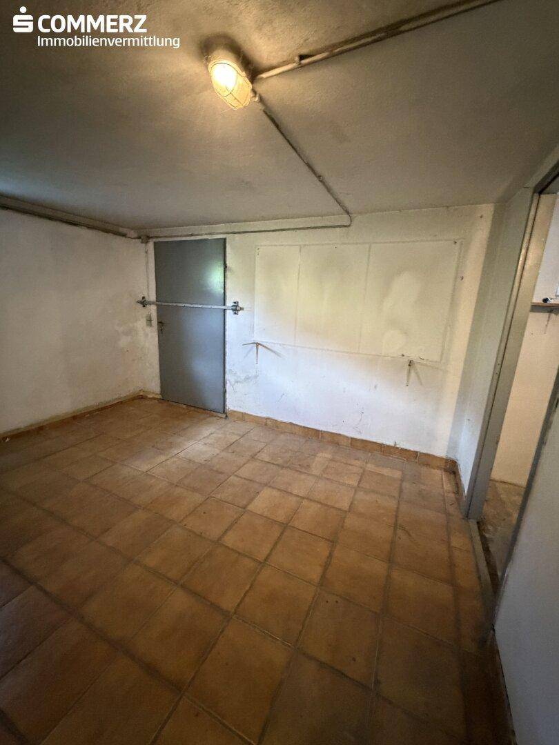 Kellerraum mit Fliesenboden und Zugang zu einem weiteren Bereich.