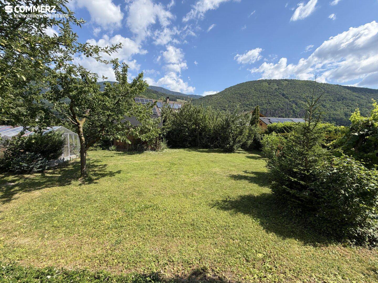 Großer, gepflegter Rasenbereich mit Obstbäumen und Blick auf die umliegenden grünen Berge.