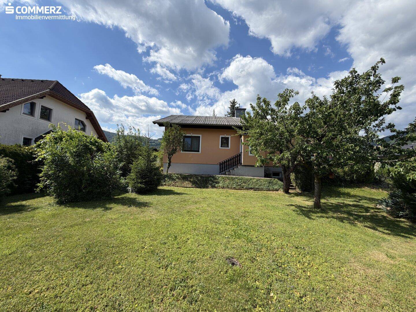 Einfamilienhaus von der Gartenseite gesehen, umgeben von Rasen und Bäumen.