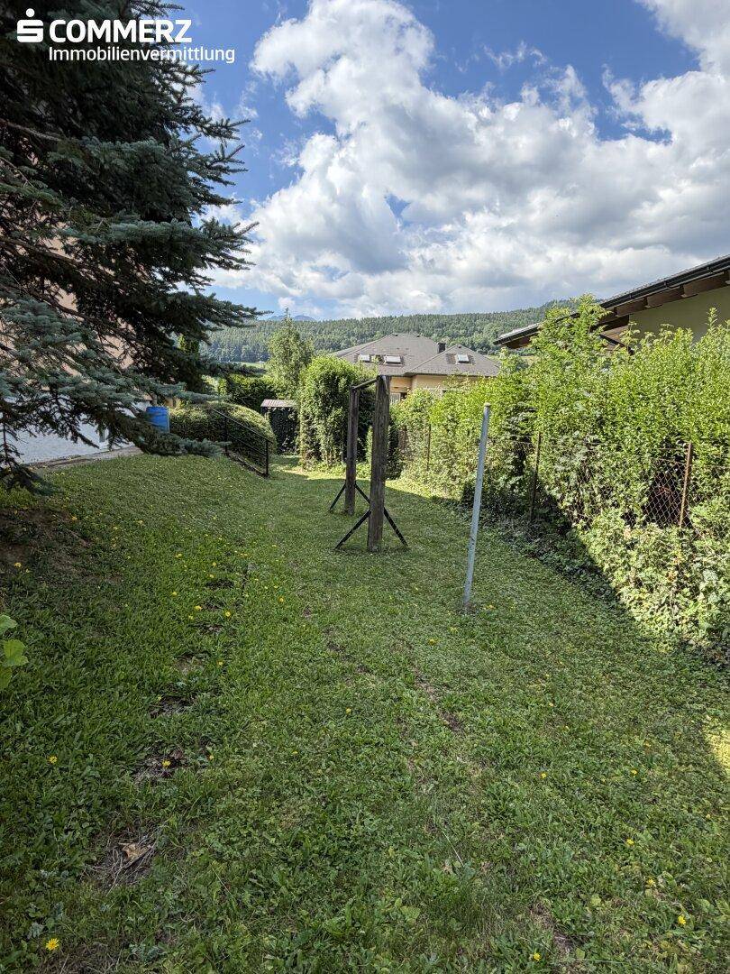 Großer Gartenbereich mit Rasen, Hecken und einem Schaukelgestell.