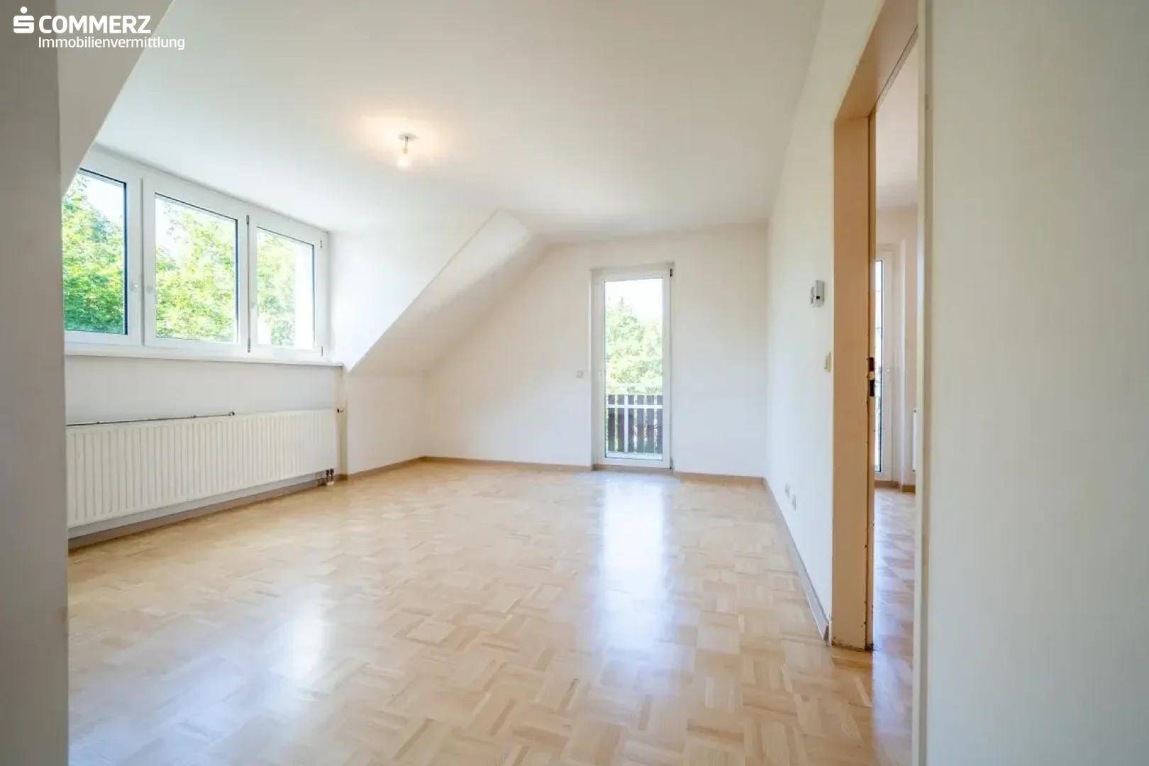 Helles Dachgeschosszimmer mit Parkettboden, Dachschräge und Zugang zu einem französischen Balkon.