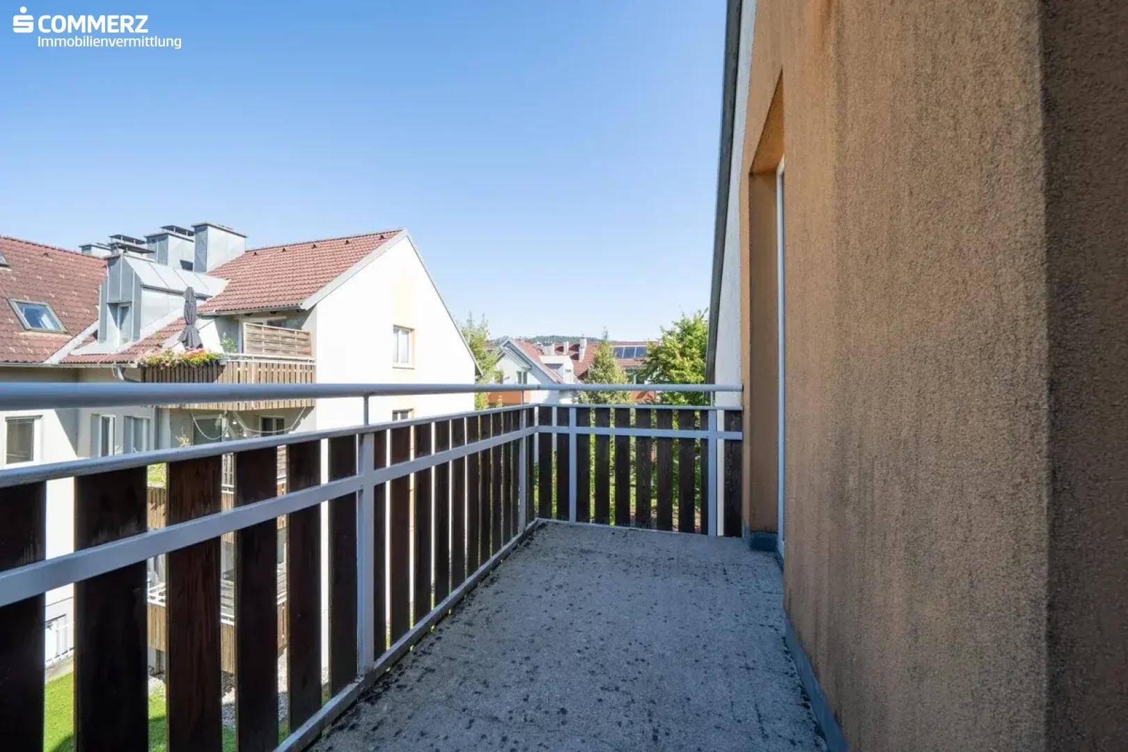 Kleiner Balkon mit Metallgeländer und Blick auf die umliegenden Häuser und Bäume.