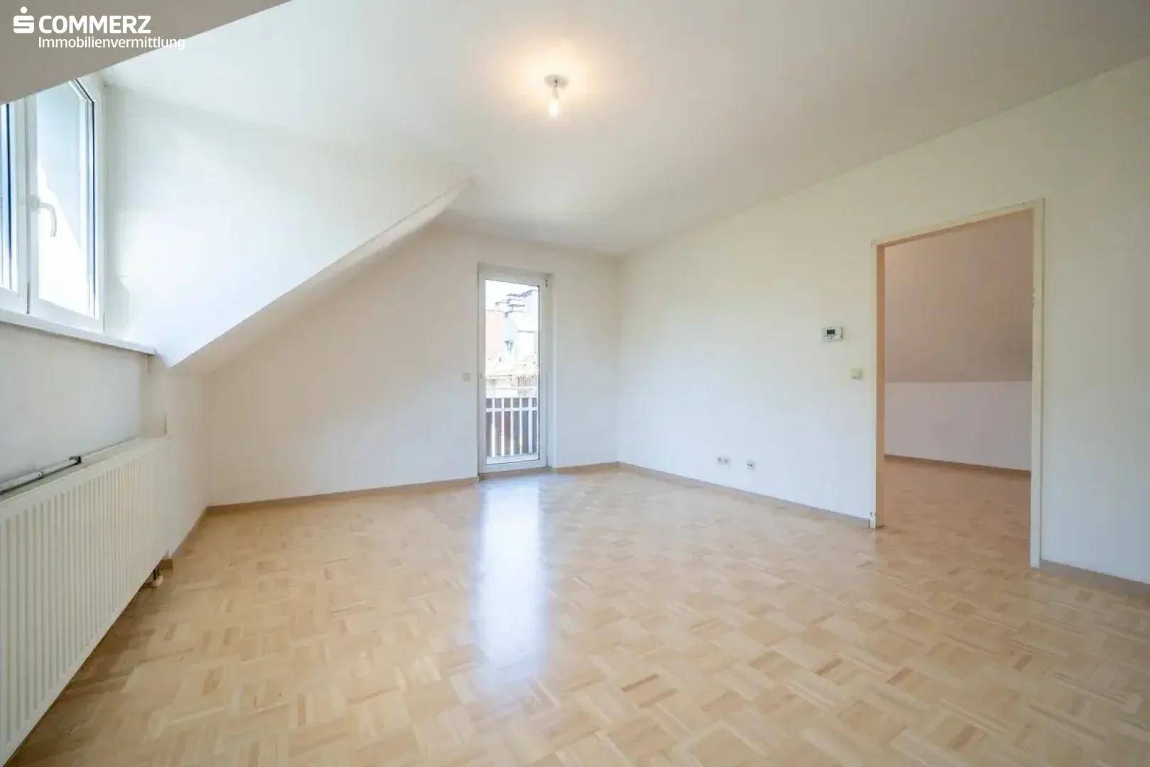 Helles Dachgeschosszimmer mit Parkettboden, Heizkörper und Zugang zu einem französischen Balkon.