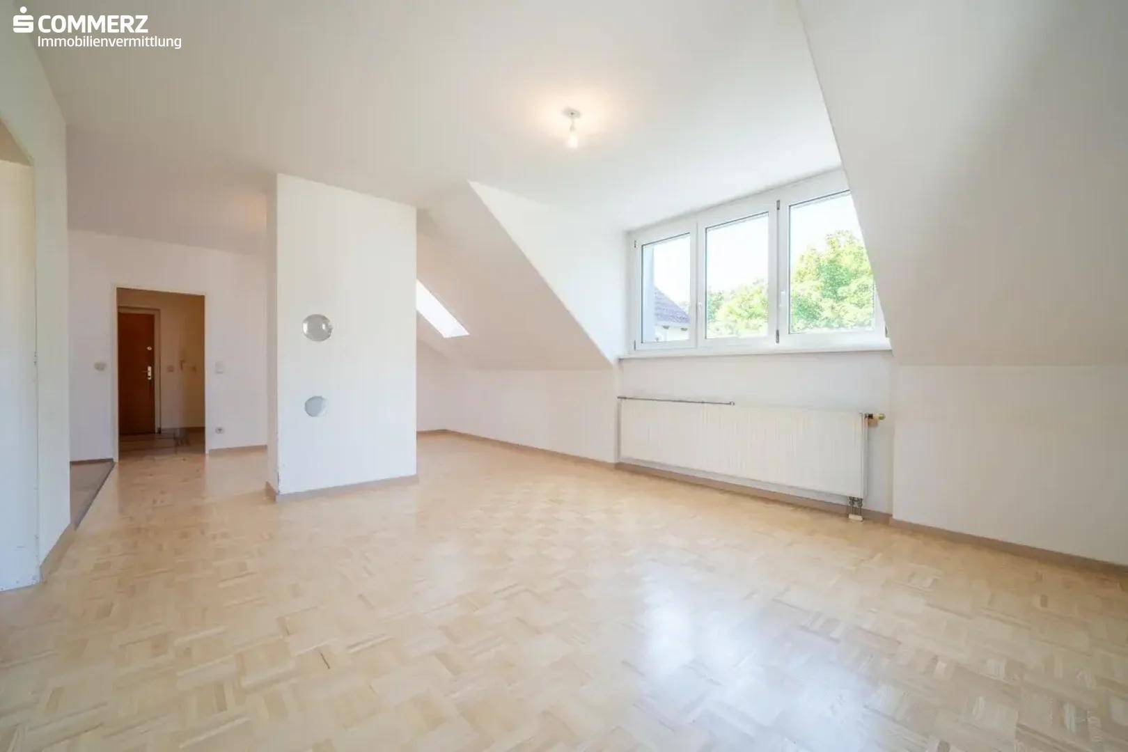 Geräumiges Dachgeschosszimmer mit Parkettboden, Dachschräge und großen Fenstern.