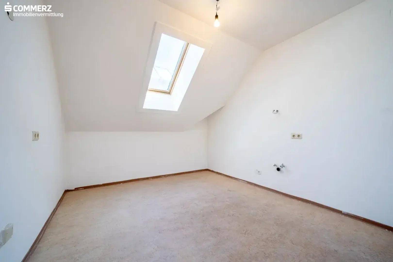 Dachgeschosszimmer mit Teppichboden, Dachfenster und Steckdosen an den Wänden.
