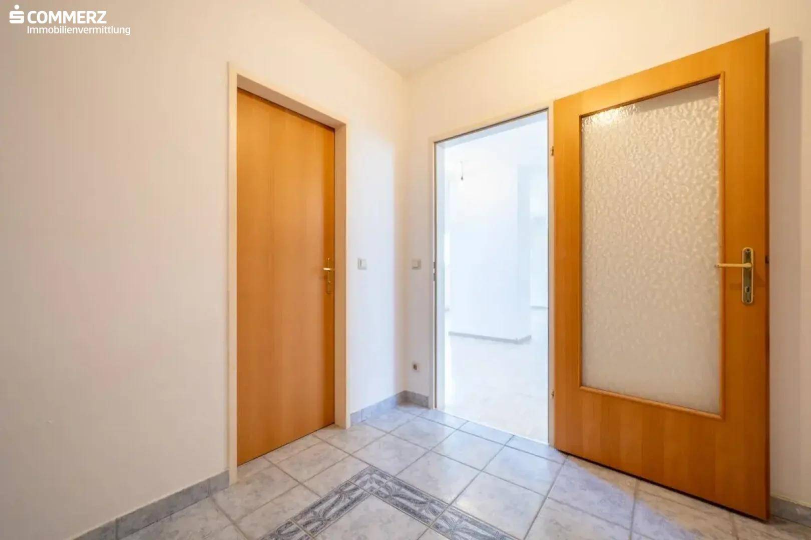 Heller Flur mit Fliesenboden und Holztüren, der zu weiteren Räumen führt.