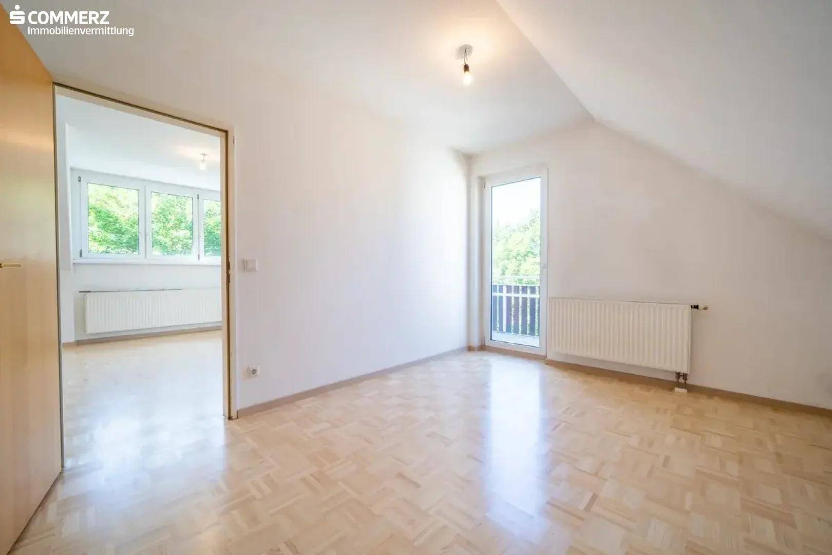 Helles Dachgeschosszimmer mit Parkettboden, Heizkörper und Zugang zu einem französischen Balkon.