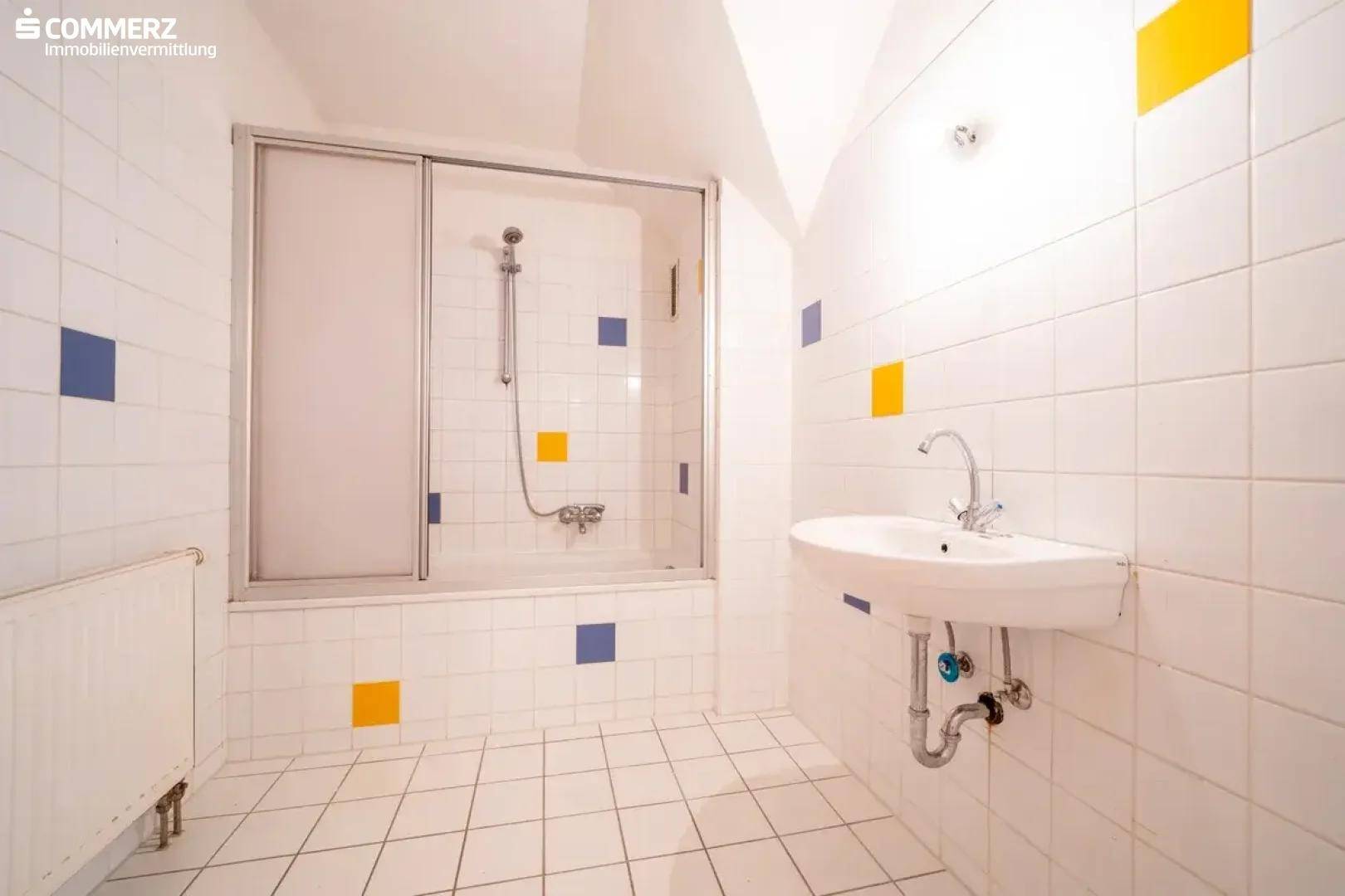 Badezimmer mit Badewanne, Duschabtrennung, Waschbecken und farbigen Fliesenakzenten.