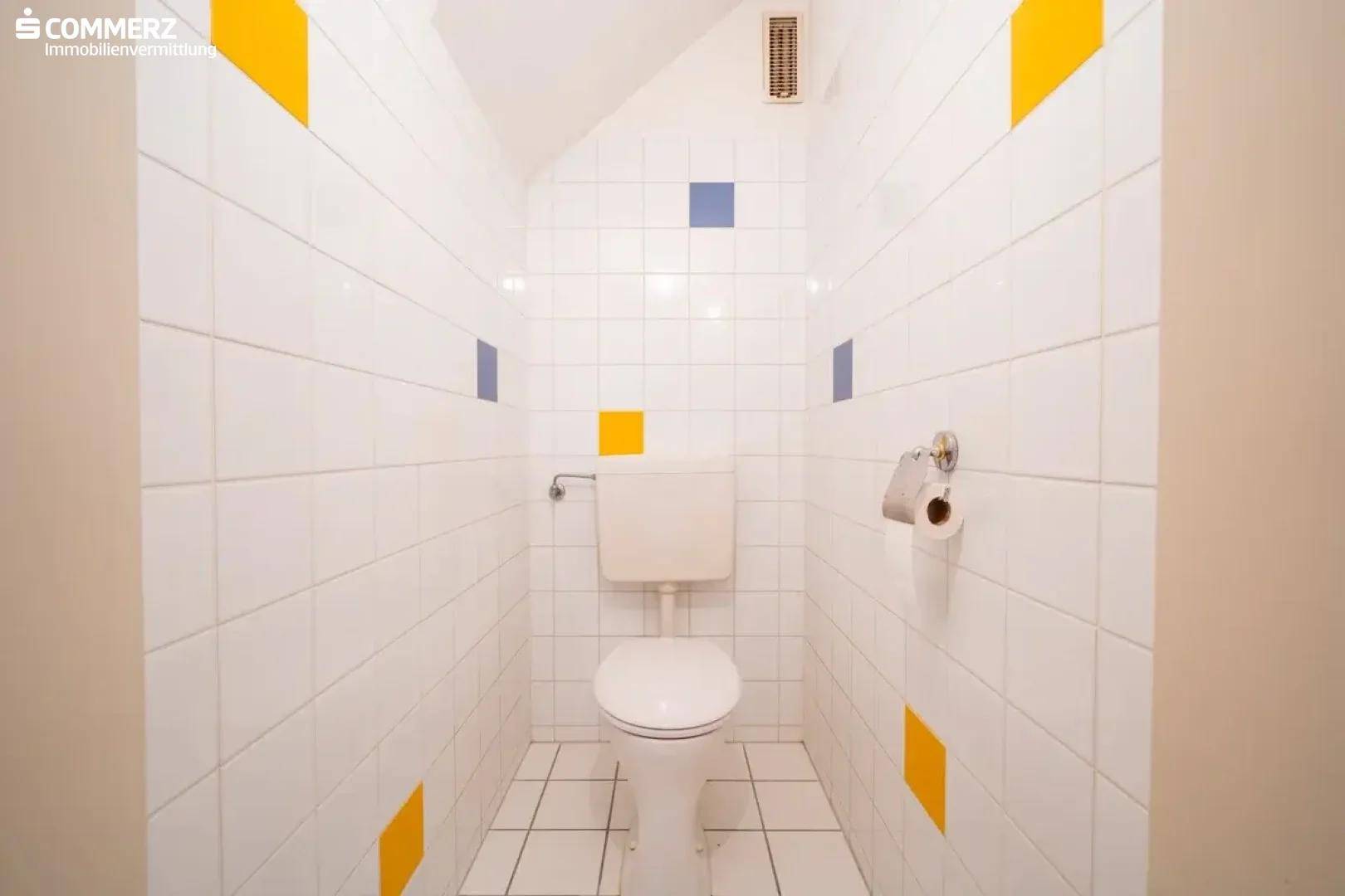 Separates WC mit weißen Fliesen und farbigen Akzenten, ausgestattet mit einer Toilette.