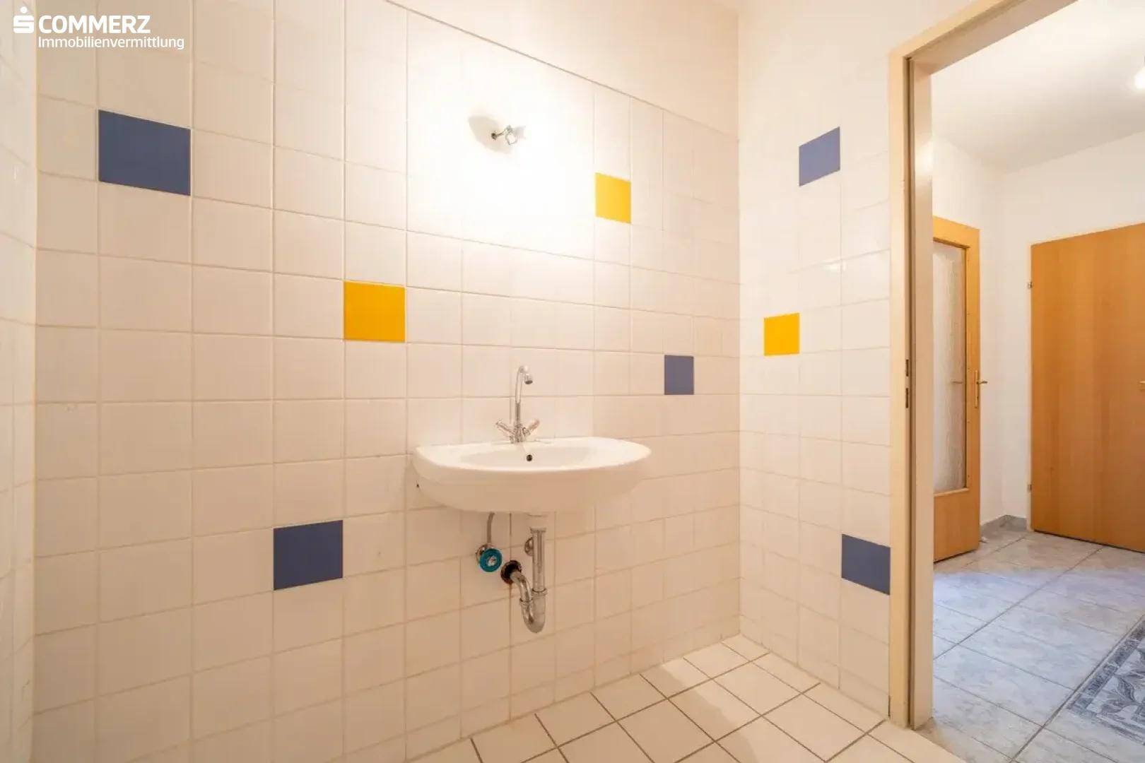 Badezimmer mit Waschbecken, weißen Fliesen und farbigen Akzenten an den Wänden.