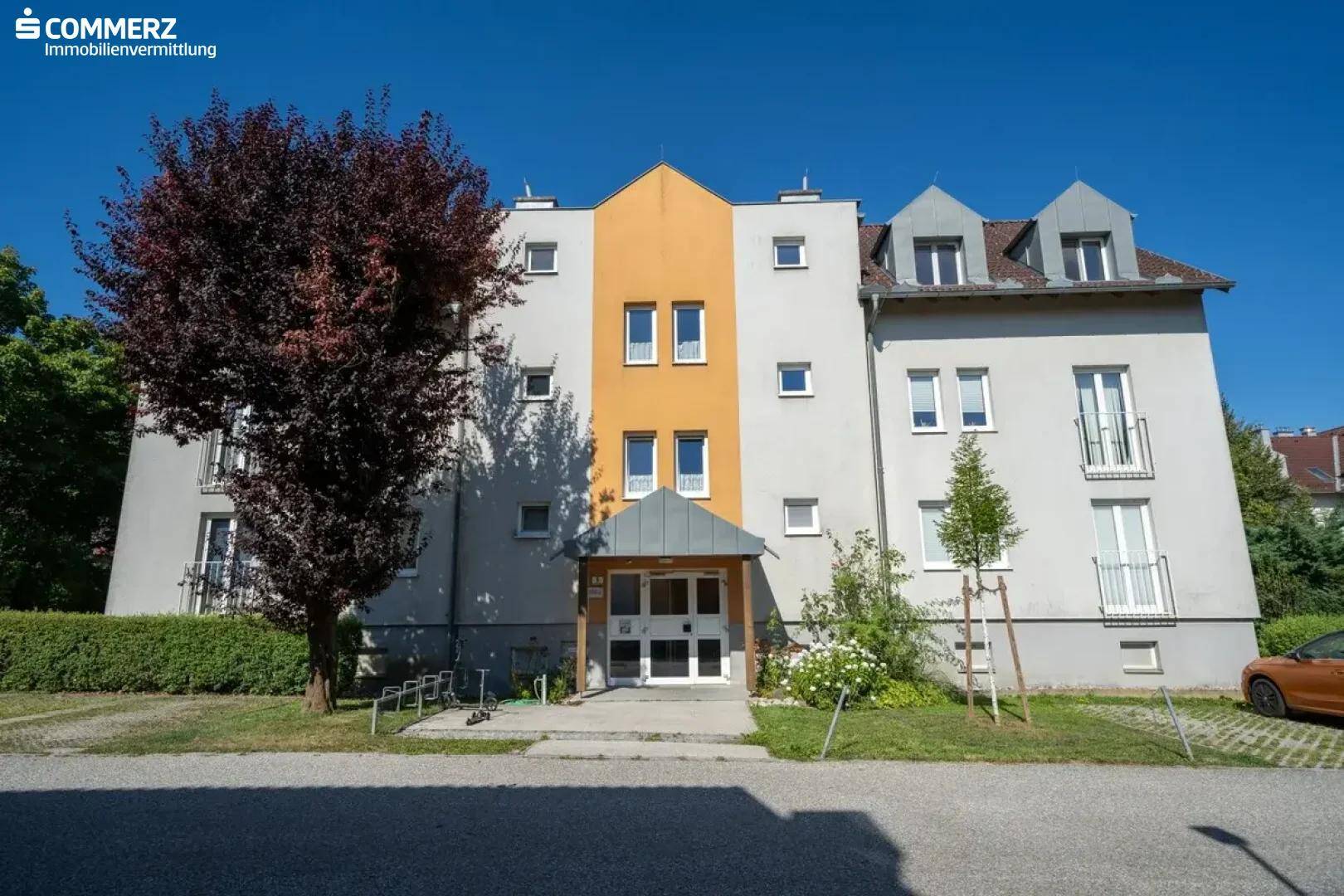 Mehrfamilienhaus mit heller Fassade und gepflegtem Eingangsbereich unter blauem Himmel.