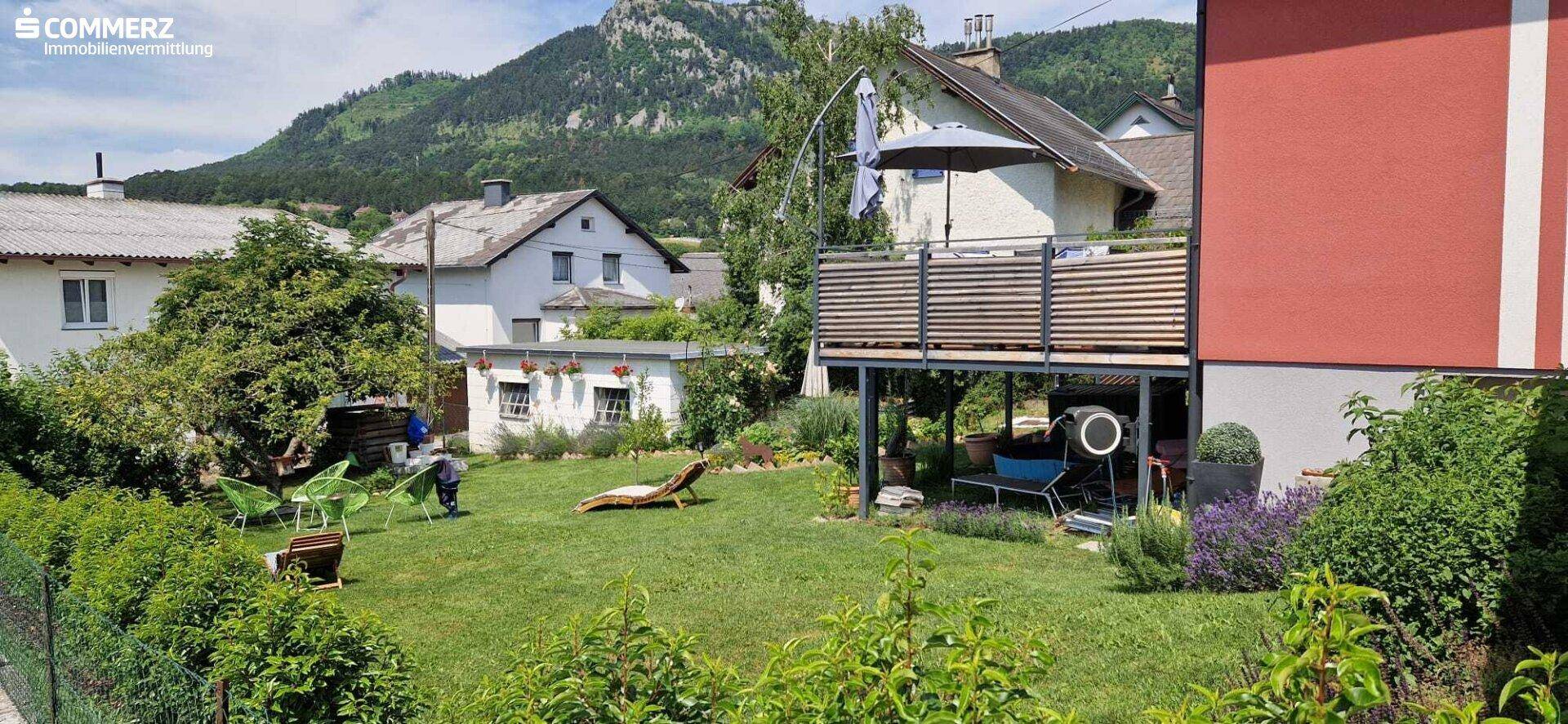 Großer Garten mit Rasenfläche, Liegestuhl und Blick auf das Haus und die umliegenden Berge.