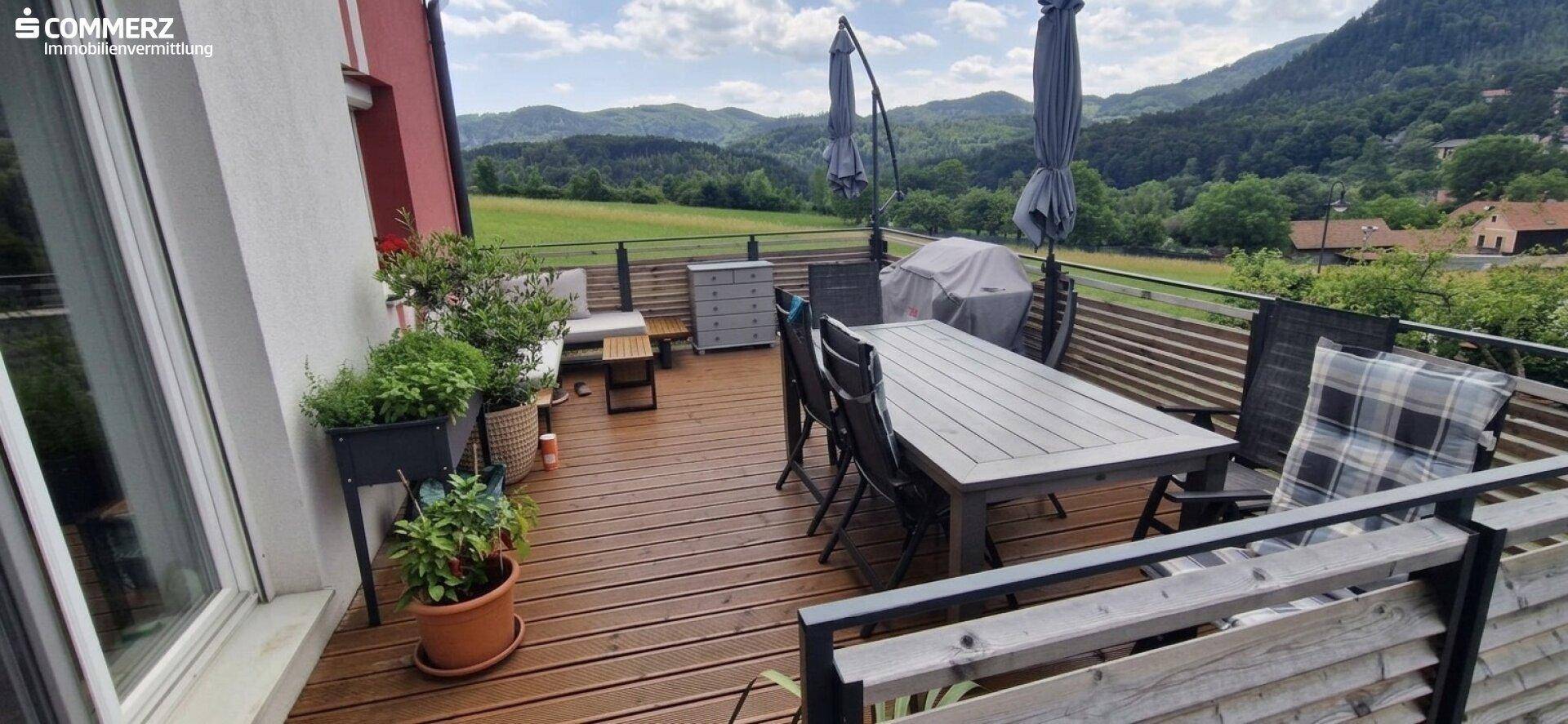 Geräumiger Holzbalkon mit Esstisch und Stühlen, ideal für Mahlzeiten im Freien mit Bergblick.