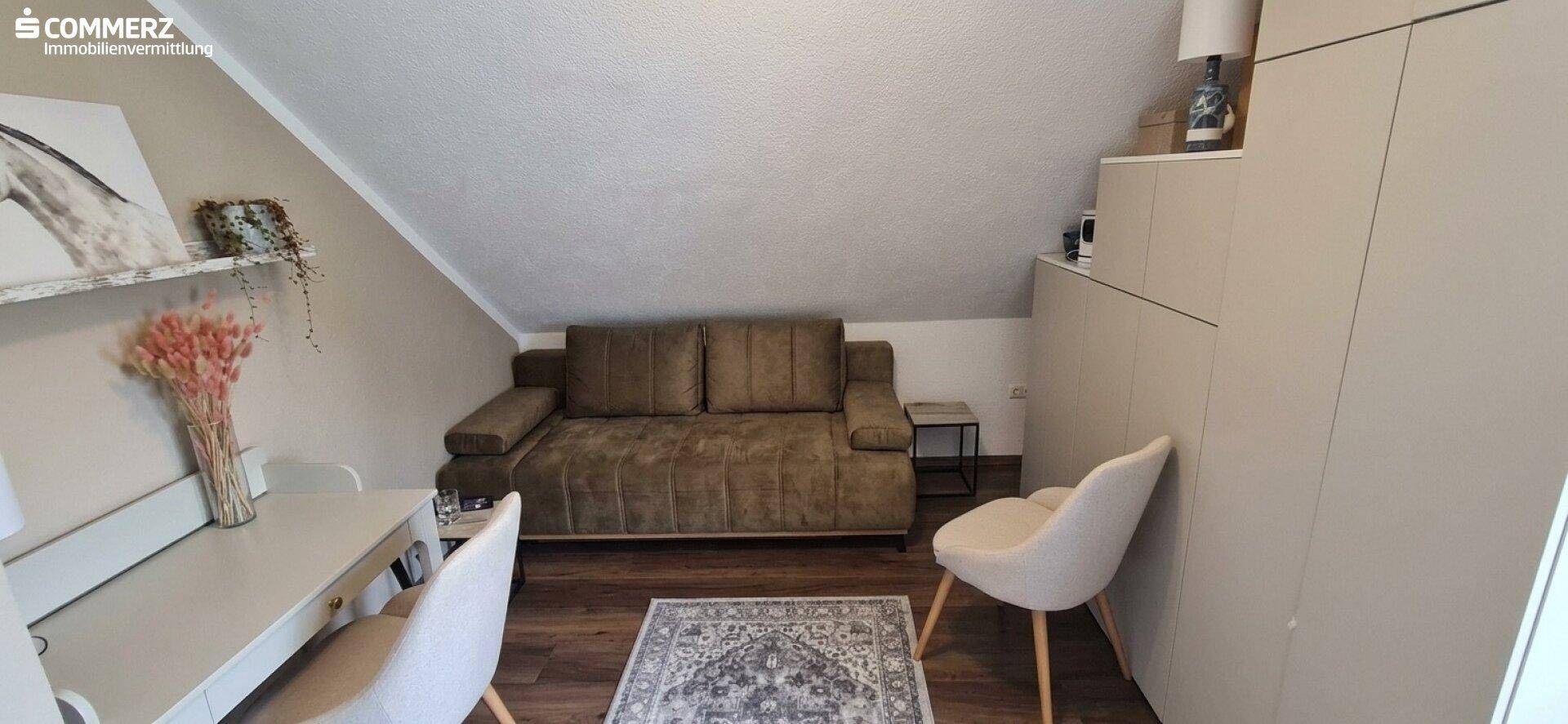 Gemütlicher Wohnbereich im Dachgeschoss mit Sofa, Teppich und schrägen Wänden.