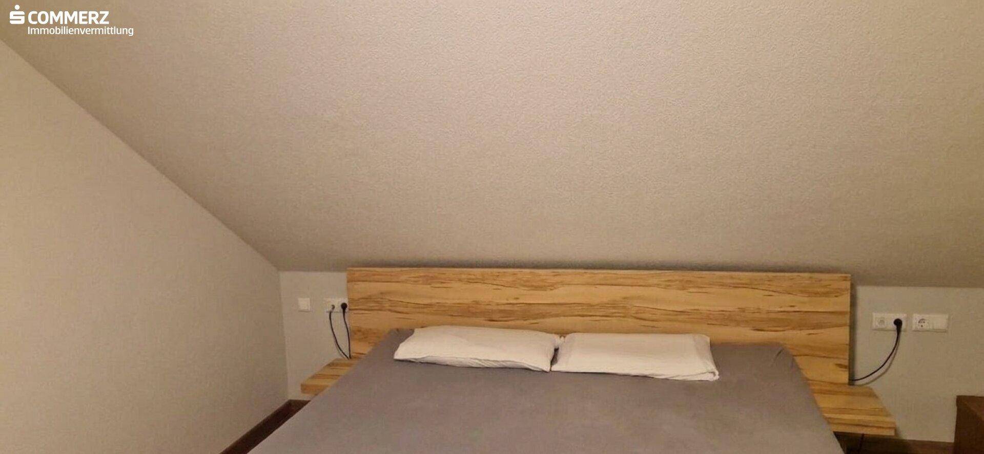 Schlafzimmer im Dachgeschoss mit Holzbett, schrägen Wänden und minimalistischer Einrichtung.