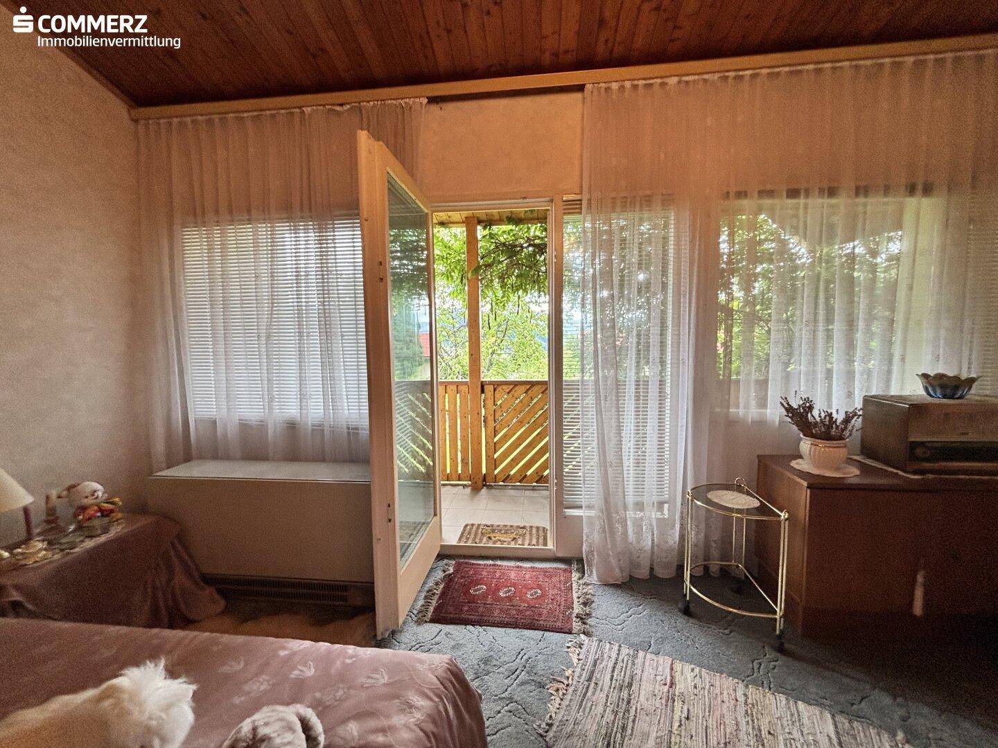 Schlafzimmer mit Holzbalkendecke, großen Fenstern und direktem Zugang zum Balkon.
