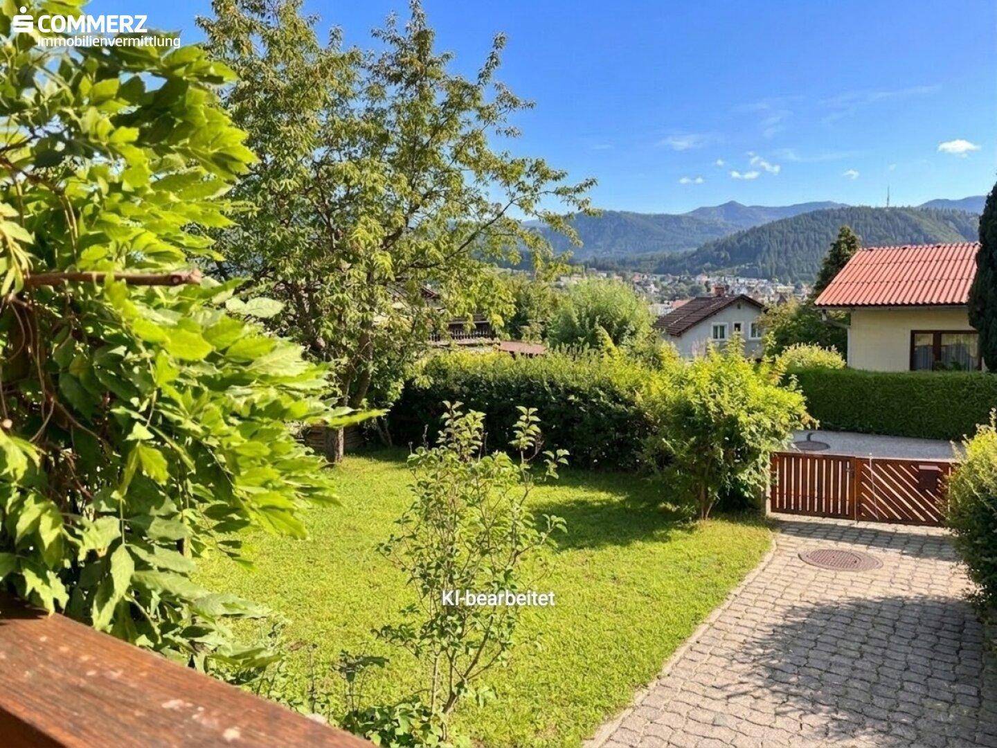 Sonniger Garten mit Rasenfläche und weitem Blick über das Tal und die umliegende Berglandschaft.